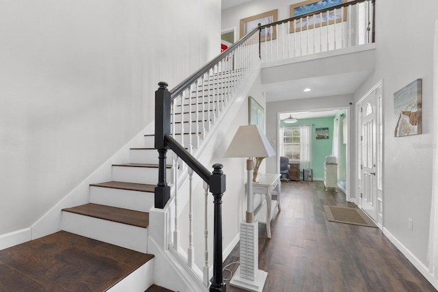 stairway with wood-type flooring and a towering ceiling