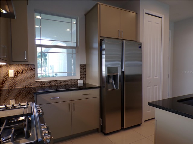 kitchen with appliances with stainless steel finishes, tasteful backsplash, light tile patterned flooring, and dark stone counters