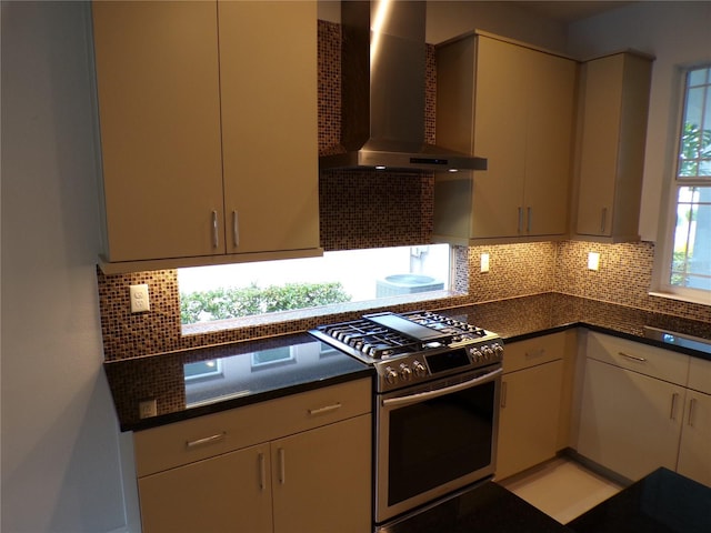 kitchen featuring tasteful backsplash, wall chimney range hood, dark stone counters, and stainless steel gas stove