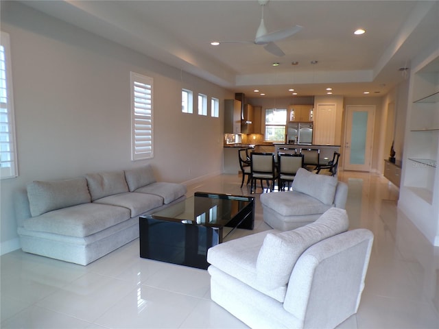 tiled living room with ceiling fan and a tray ceiling