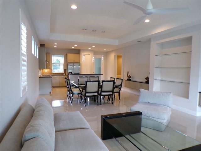 living room with a raised ceiling, ceiling fan, and light tile patterned floors