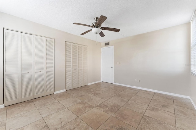 unfurnished bedroom featuring a textured ceiling, two closets, light tile patterned floors, and ceiling fan