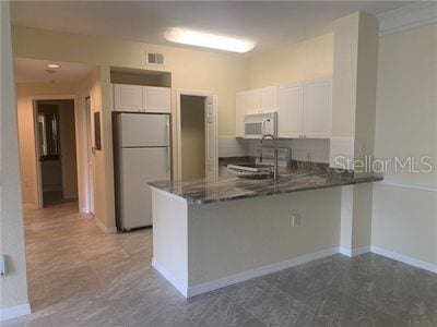 kitchen featuring white appliances, kitchen peninsula, sink, and white cabinets