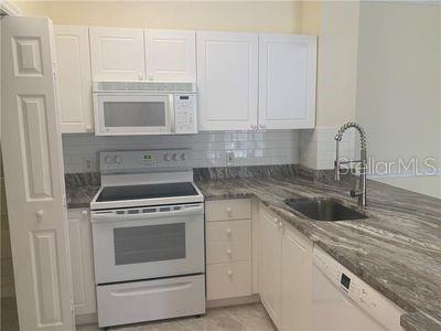 kitchen featuring white cabinets, white appliances, dark stone countertops, and sink