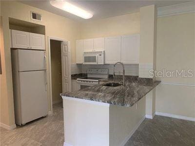 kitchen featuring white cabinets, sink, kitchen peninsula, white appliances, and dark stone counters