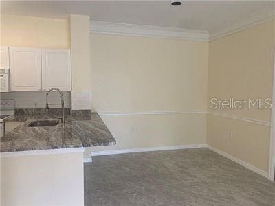 kitchen with white cabinets, sink, kitchen peninsula, dark stone countertops, and crown molding