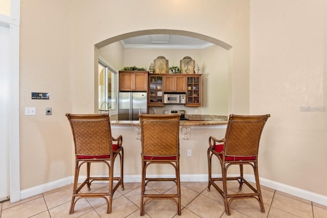 bar featuring light stone counters, light tile patterned floors, appliances with stainless steel finishes, and ornamental molding