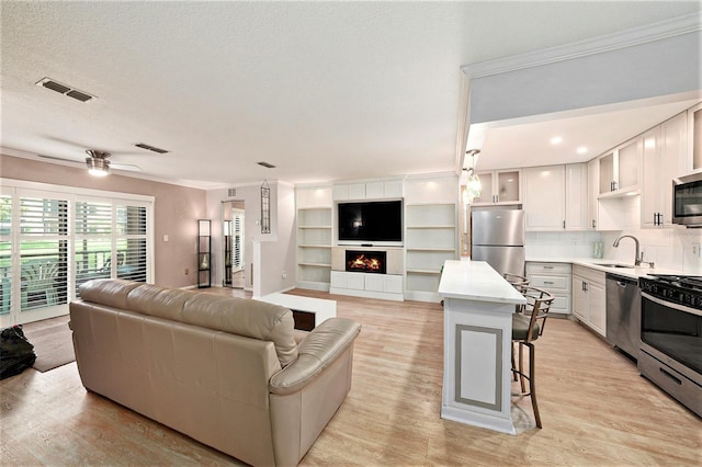 living room with crown molding, sink, ceiling fan, light wood-type flooring, and a textured ceiling