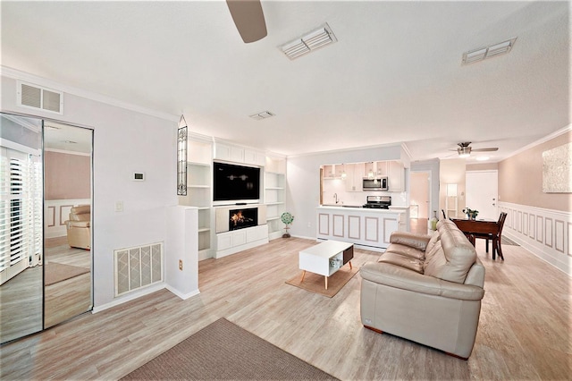 living room with ceiling fan, light hardwood / wood-style floors, built in features, and ornamental molding