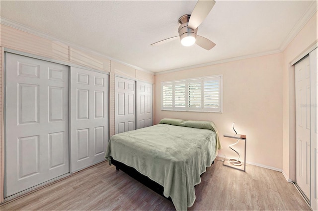 bedroom featuring ceiling fan, light hardwood / wood-style floors, crown molding, and multiple closets