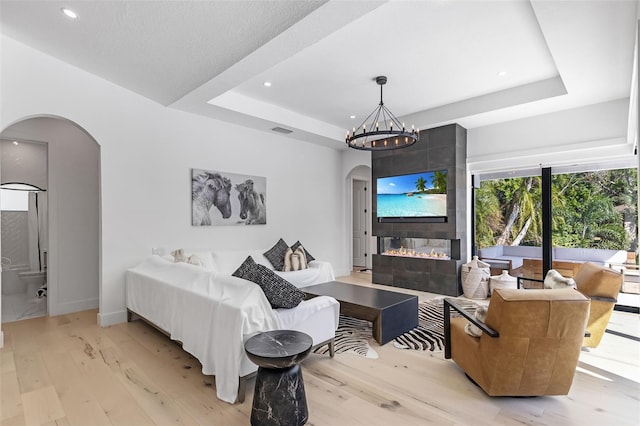 living room with an inviting chandelier, light hardwood / wood-style flooring, a fireplace, and a raised ceiling