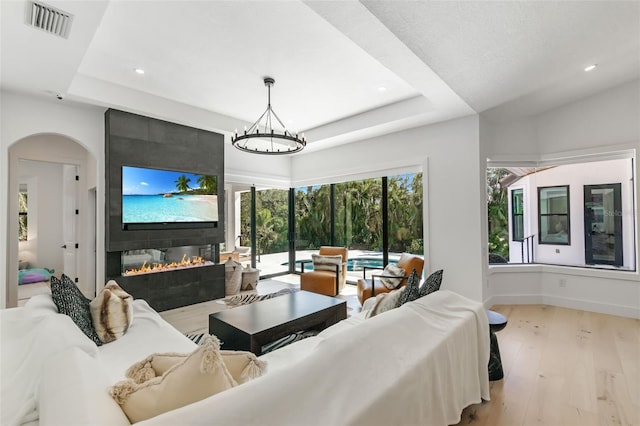 living room with light hardwood / wood-style floors, a fireplace, a tray ceiling, and a notable chandelier