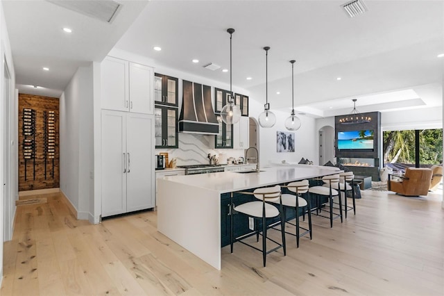 kitchen with pendant lighting, a center island with sink, light hardwood / wood-style floors, and wall chimney range hood