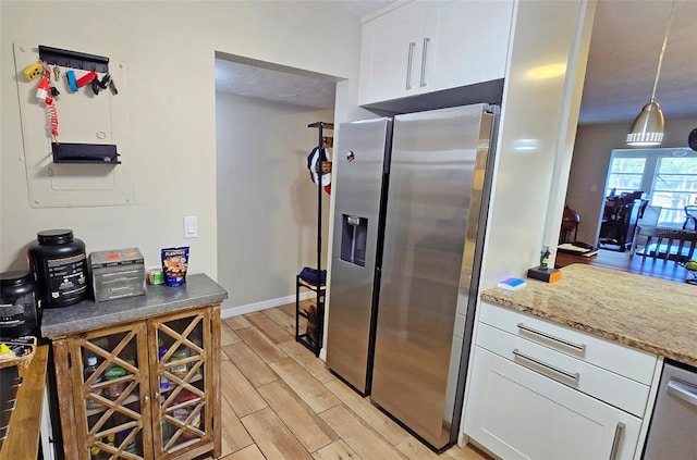 kitchen with appliances with stainless steel finishes, decorative light fixtures, white cabinetry, and light hardwood / wood-style floors