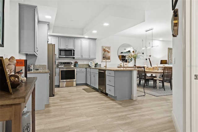 kitchen with gray cabinetry, stainless steel appliances, kitchen peninsula, light hardwood / wood-style floors, and decorative light fixtures