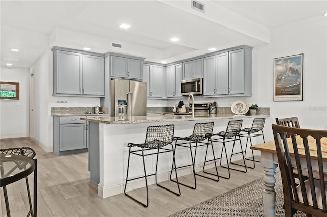 kitchen with kitchen peninsula, light stone counters, gray cabinetry, stainless steel appliances, and light hardwood / wood-style flooring