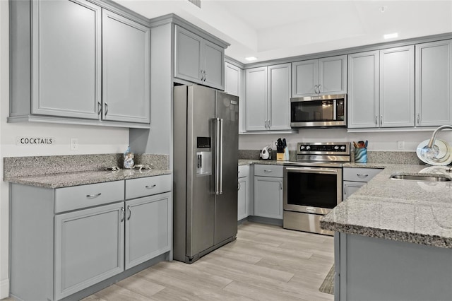 kitchen featuring appliances with stainless steel finishes, light wood-type flooring, light stone counters, sink, and gray cabinets