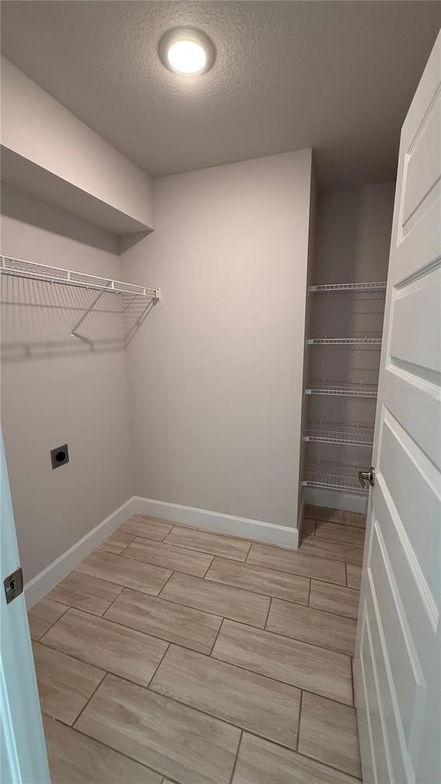 laundry room featuring laundry area, baseboards, wood finish floors, a textured ceiling, and hookup for an electric dryer