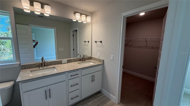 full bathroom with double vanity, toilet, a walk in closet, and a sink