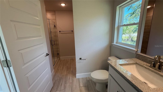 bathroom featuring vanity, toilet, baseboards, wood tiled floor, and a shower stall