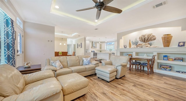 living room with crown molding, light hardwood / wood-style floors, a tray ceiling, and ceiling fan