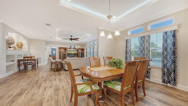 dining room with ceiling fan with notable chandelier, crown molding, a tray ceiling, and light hardwood / wood-style flooring