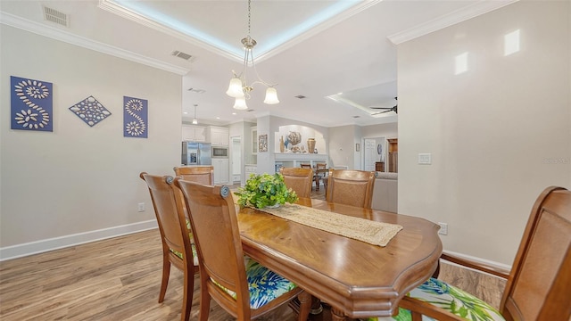 dining area featuring ceiling fan with notable chandelier, light hardwood / wood-style flooring, a raised ceiling, and ornamental molding