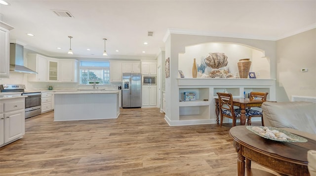 kitchen featuring hanging light fixtures, white cabinets, wall chimney exhaust hood, stainless steel appliances, and light hardwood / wood-style flooring