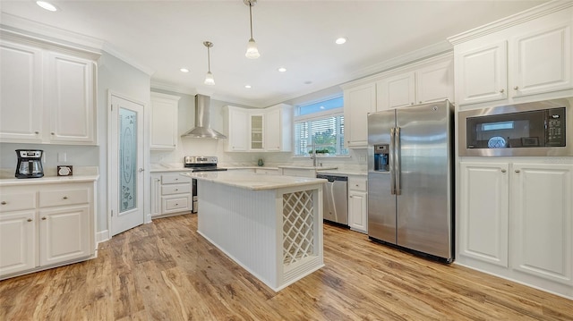 kitchen featuring white cabinets, wall chimney exhaust hood, light hardwood / wood-style flooring, decorative light fixtures, and stainless steel appliances