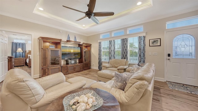 living room with crown molding, a raised ceiling, ceiling fan, and light wood-type flooring