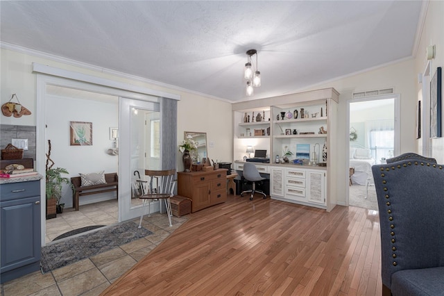 office space featuring light wood-type flooring, built in desk, ornamental molding, and built in features