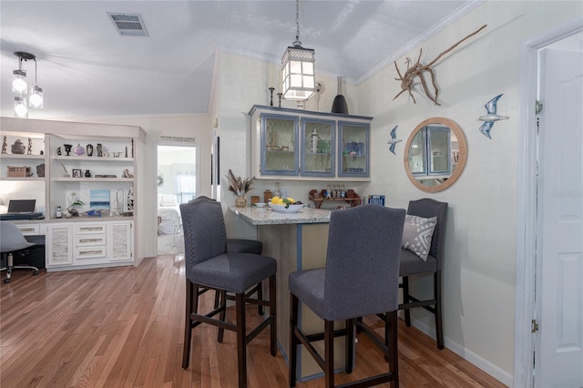 dining room featuring light wood-type flooring, lofted ceiling, ornamental molding, and built in desk