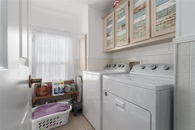 clothes washing area with cabinets, tile walls, washing machine and clothes dryer, and light tile patterned floors