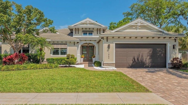 view of front facade with stucco siding, french doors, decorative driveway, an attached garage, and a front lawn