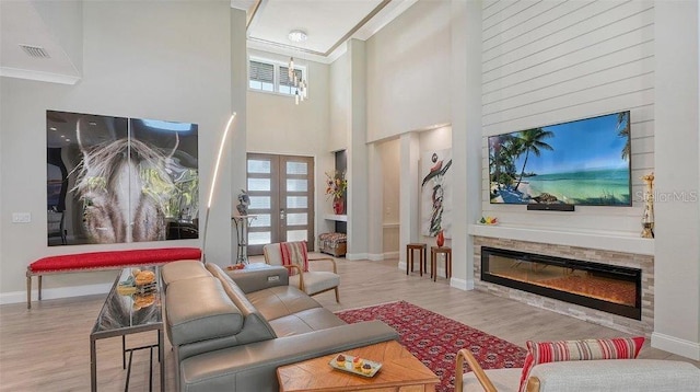 living room with a glass covered fireplace, baseboards, ornamental molding, a high ceiling, and wood finished floors
