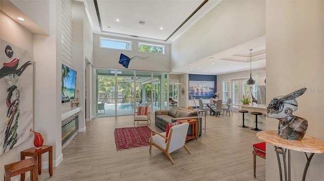 living room featuring ornamental molding, light wood-style flooring, a towering ceiling, and a healthy amount of sunlight