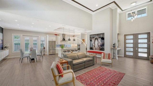 living room with light wood-type flooring, a towering ceiling, and french doors