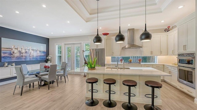 kitchen featuring wall chimney exhaust hood, stainless steel appliances, light hardwood / wood-style flooring, and decorative light fixtures