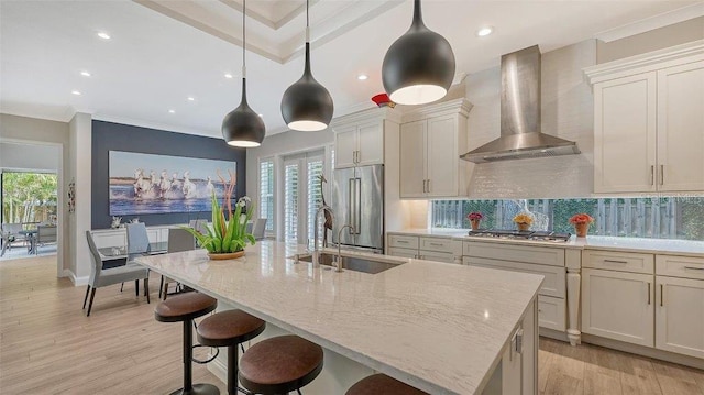 kitchen with light wood-type flooring, wall chimney range hood, a sink, stainless steel appliances, and backsplash