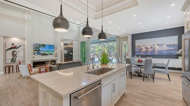 kitchen with a kitchen island with sink, sink, white cabinetry, hanging light fixtures, and stainless steel dishwasher