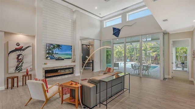 living area with a sunroom, wood finished floors, a high ceiling, and a glass covered fireplace