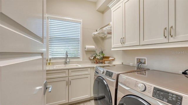 clothes washing area with washer and clothes dryer, cabinets, light hardwood / wood-style flooring, and sink