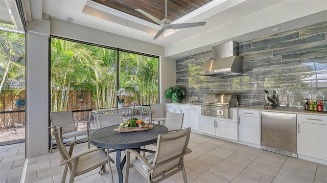 interior space with tasteful backsplash, fridge, wall chimney exhaust hood, and a raised ceiling