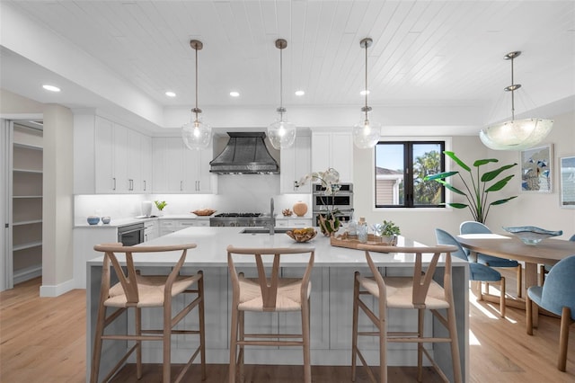 kitchen featuring custom range hood, light wood-type flooring, white cabinetry, and hanging light fixtures