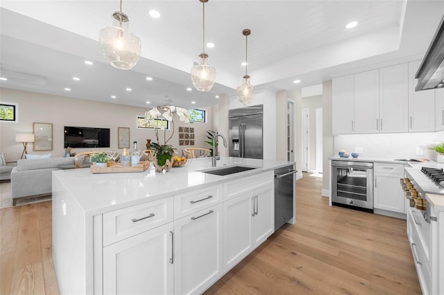 kitchen featuring beverage cooler, a center island with sink, light hardwood / wood-style flooring, high quality appliances, and white cabinetry