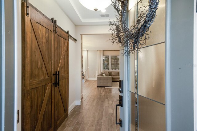 corridor with a tray ceiling, a barn door, and hardwood / wood-style floors