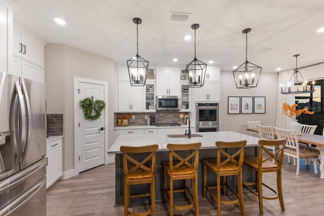 kitchen with stainless steel appliances, a center island with sink, hanging light fixtures, and light wood-type flooring