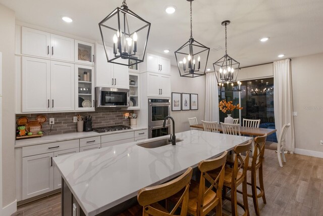 kitchen with appliances with stainless steel finishes, white cabinetry, sink, and an island with sink