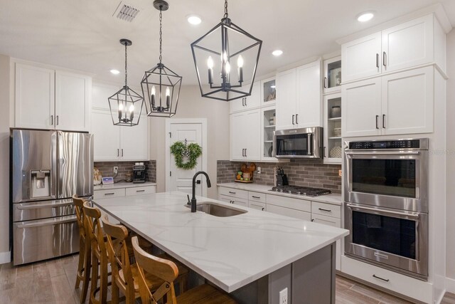 kitchen with sink, an island with sink, stainless steel appliances, hardwood / wood-style floors, and decorative light fixtures