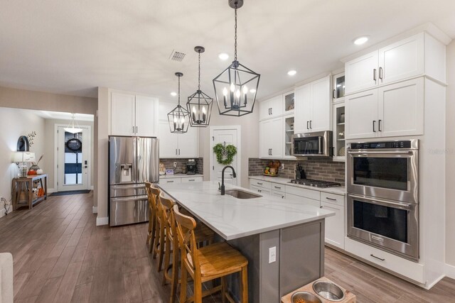 kitchen featuring appliances with stainless steel finishes, white cabinetry, an island with sink, wood-type flooring, and sink